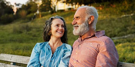 Una pareja de adultos mayores luce feliz mientras habla en un banco al aire libre