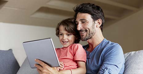 Padre e hijo felices usando una tableta digital en un sofá, en casa