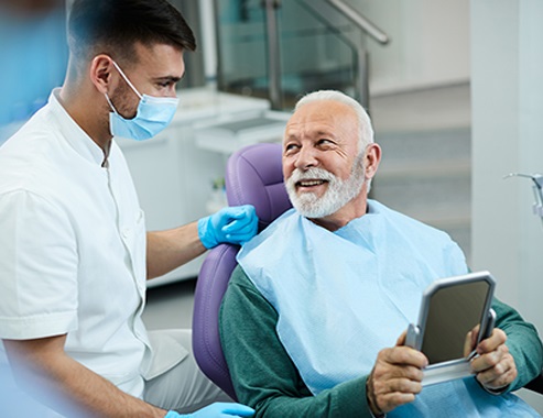 Hombre mayor contento hablando con su dentista mientras está satisfecho con el procedimiento dental en el consultorio del dentista.